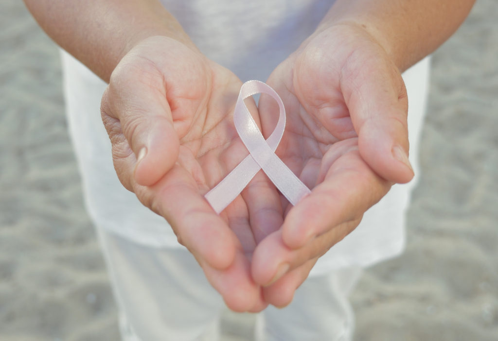 Pair of open human hands close up in front of person with light pink ribbon symbol of surviving breast cancer